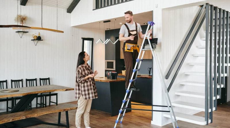Artisan du bâtiment sur un escabeau expliquant le projet pour rénover sa maison à Montpellier à une cliente dans un salon moderne