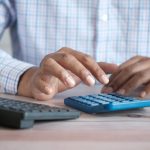 person using calculator at desk with coffee mug
