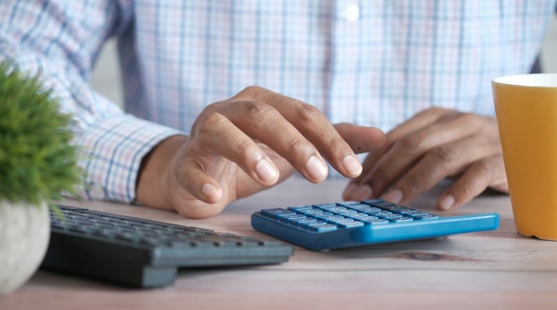 person using calculator at desk with coffee mug